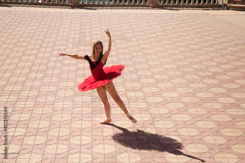 Classical ballet dancer dancing in the street. The dancer is wearing a red tutu and is performing a classical work from Spain, Carmen. You can see the shadows of the dancer on the floor. 