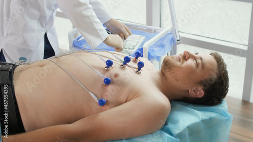Electrocardiogram Procedure for Diagnosing Heart Disease. A Cardiologist Puts Electrodes on the Bare Chest of a Young Man Lying on the Couch To Take an Electrocardiogram in the Clinic S Office.