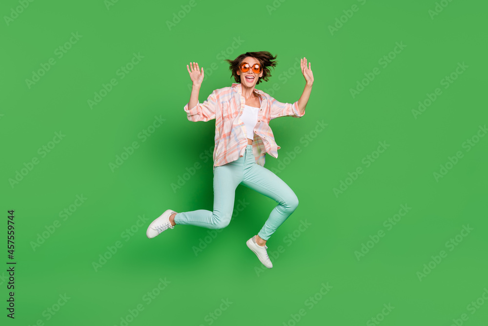 Full length photo of cheerful positive happy woman jump up wear summer cool sunglass isolated on green color background
