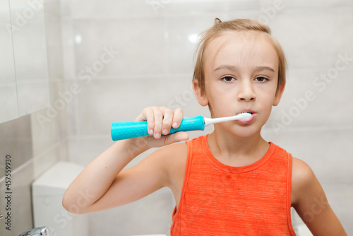 Kid brushing teeth with electic brush in bathroom. Dental hygiene every day. Happy boy cleaning teeth.