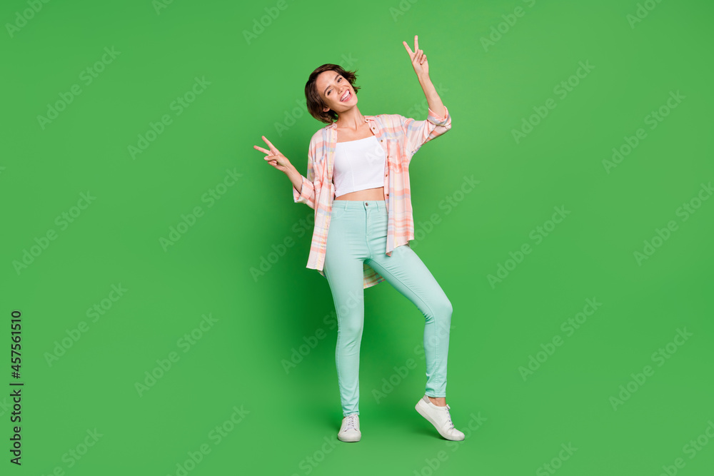 Full length photo of cheerful positive happy young woman hand show v-signs isolated on green color background Full length photo of cheerful positive happy young woman hand show v-signs isolated on green color background