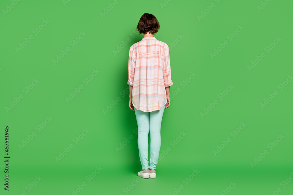 Full length back rear side spine view photo of young woman wear casual clothes plaid shirt isolated on green color background Full length back rear side spine view photo of young woman wear casual clothes plaid shirt isolated on green color background