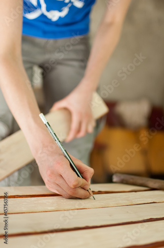 Female hands are making some marks on wooden plank for future holes using pencil for assembling bench, gender equality, feminism, do it yourself concepts.