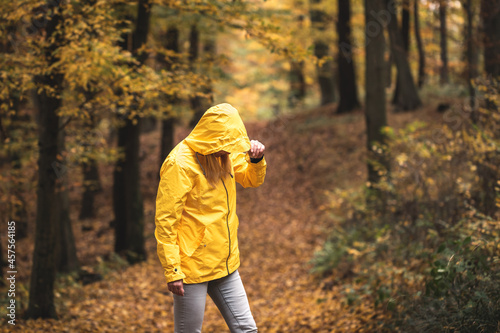 Hiker in autumn forest. Female tourist wearing yellow jacket with hood in cold weather. Wanderlust in woodland at fall season