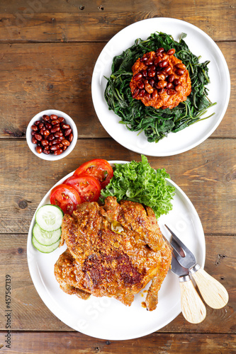 Ayam bakar Taliwang is a traditional roast chicken from Lombok Indonesia on a wooden background, served with plecing.