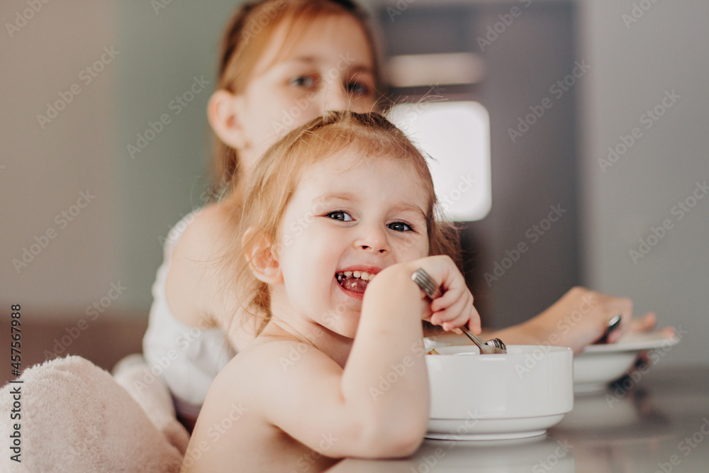 Happy children sitting at table, smiling and eating fresh cooked meal from white plates. Tasty lunch at cozy home. Happy children sitting at table, smiling and eating fresh cooked meal from white plates. Tasty lunch at cozy home.