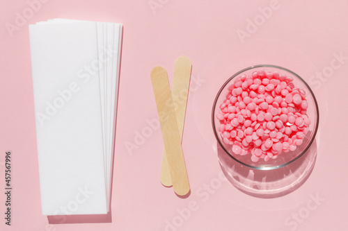 Beautiful pink depilatory wax granules, strips for depilation and wooden spatulas on a pink background. Epilation, depilation, unwanted hair removal. Top view.