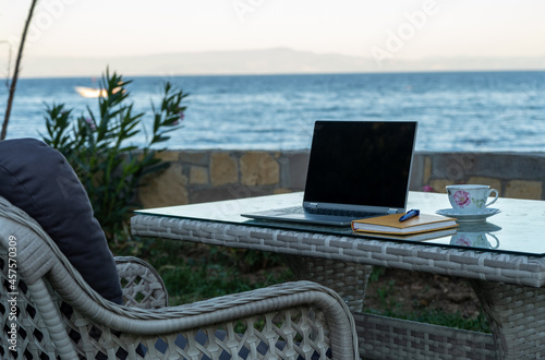 working from summer house remote concept in pandemic, table ready for work with laptop notebook pen phone near the seaside photo