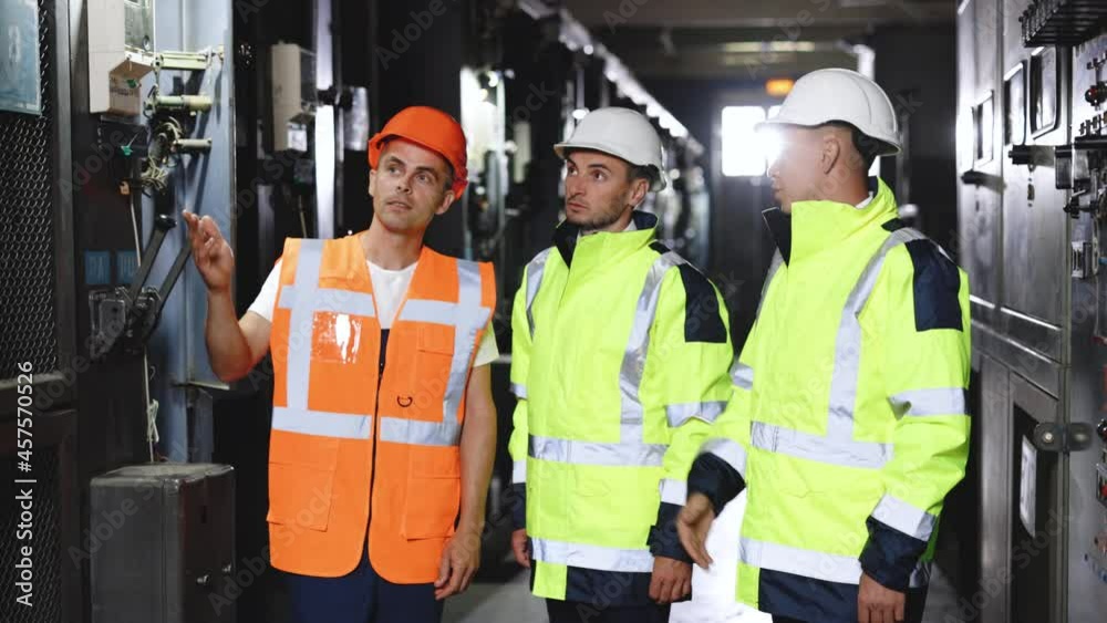 Engineers in uniform and helmets do pre-commissioning works inspecting electrical station. Group of three engineer team with perfect safety uniform brainstorming idea planning project of industry. Engineers in uniform and helmets do pre-commissioning works inspecting electrical station. Group of three engineer team with perfect safety uniform brainstorming idea planning project of industry.
