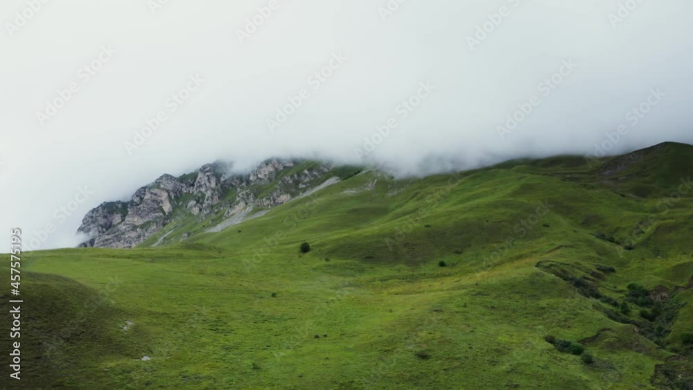 Hilly terrain, with grass with rocky mountains, the tops are covered with clouds Hilly terrain, with grass with rocky mountains, the tops are covered with clouds