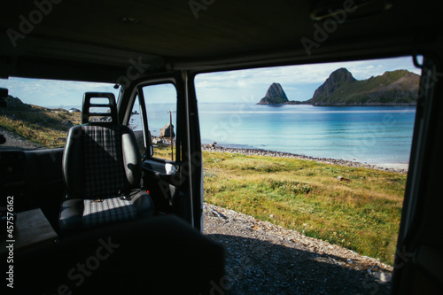 View from inside of camper van on beautiful beach with turquoise water and mountain cliffs. Adventure camping life vibes. Vanlife lifestyle in scandinavian landscape. Interior of converted camper van