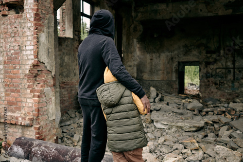 Rear view of father embracing child and looking at ruins of house after hostilities © pressmaster