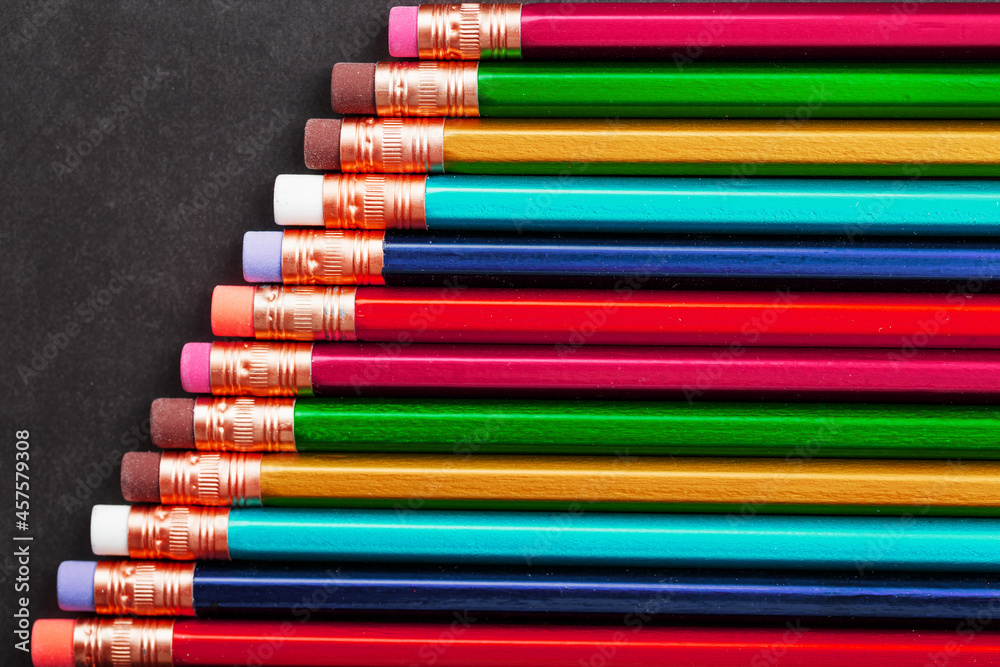 Fototapeta premium Pencils of different colors in a row on a black textured background.