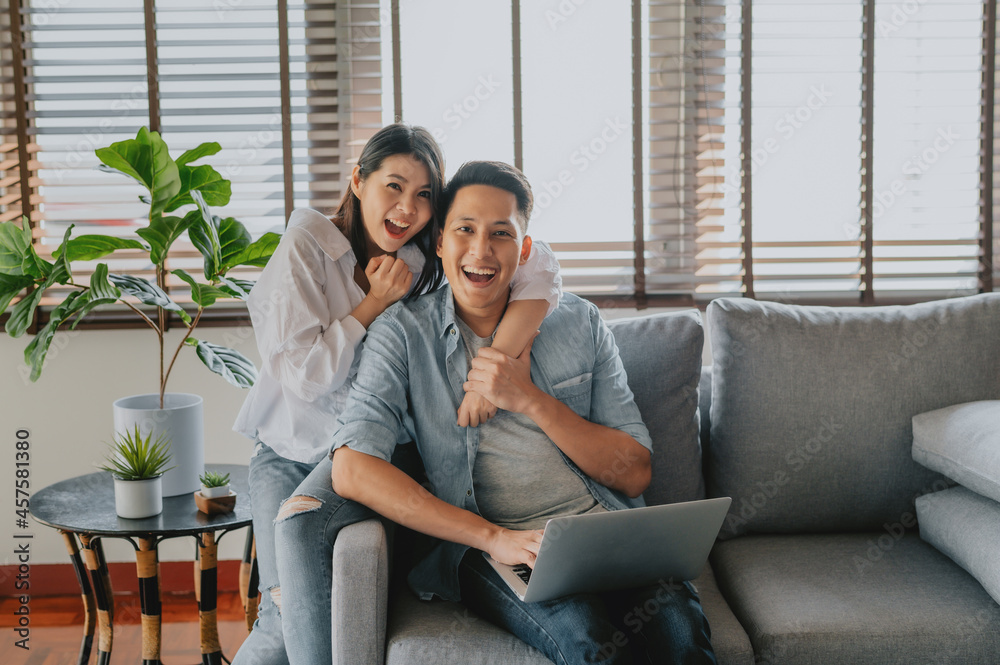 Happy Asian couple using laptop on sofa at home Happy Asian couple using laptop on sofa at home