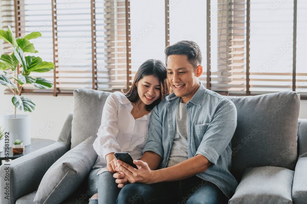 Asian couple using smartphone sitting on sofa Asian couple using smartphone sitting on sofa