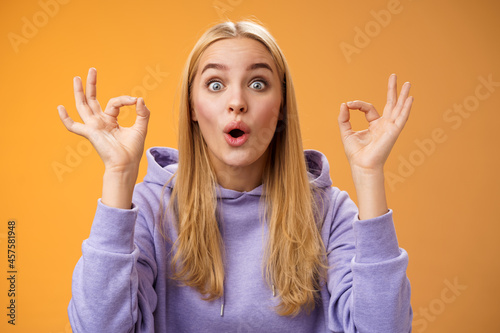 Amused talented creative young blond female tell excellent idea show okay no problem gesture persuade friends everything alright standing excited orange background ok signs, folding lips amazed photo