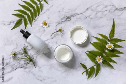 Natural cosmetic products. Daily hygiene and female healthy skincare. Cosmetic cream and skin care serum with cammomile flofers on marble countertop. SPA natural organic beauty product.