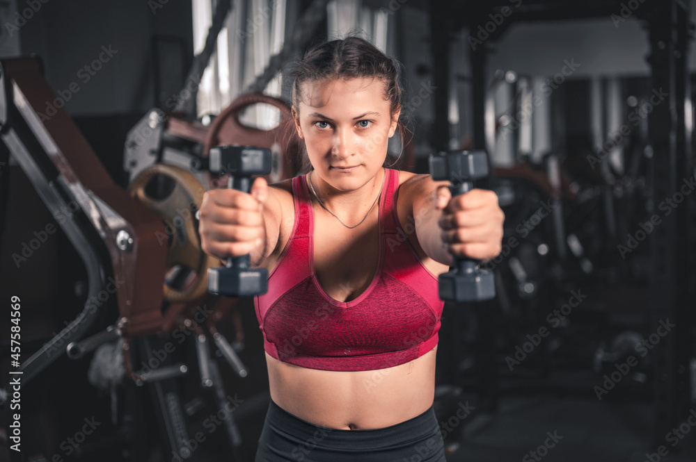 Young woman with dumbbells in the gym. Portrait of young attractive woman in sport clothes holding weight dumbbell doing fitness workout Young woman with dumbbells in the gym. Portrait of young attractive woman in sport clothes holding weight dumbbell doing fitness workout