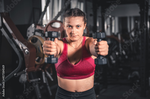 Young woman with dumbbells in the gym. Portrait of young attractive woman in sport clothes holding weight dumbbell doing fitness workout © andyborodaty