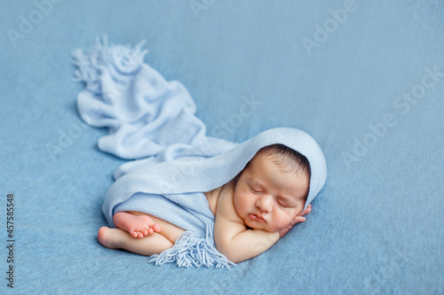 Sleeping newborn baby on a blue background covered by blanket. A few days from birth. Hands under the cheek.