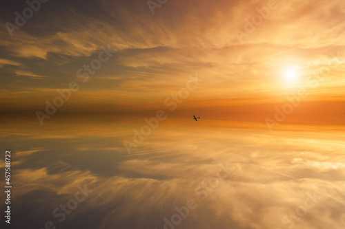 A small plane flies in the air. In the background is a beautiful colorful sky with the setting sun.