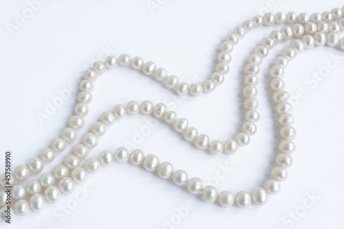 Abstract arranged three rows of natural pale pearl necklace on white paper background
