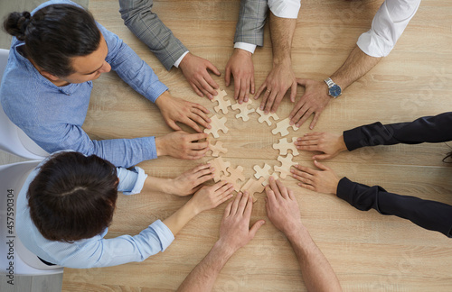 Diverse business people team group joining puzzle pieces sitting at office desk table view from top above. Collaboration and cooperation strategy, teamwork and teambuilding concept