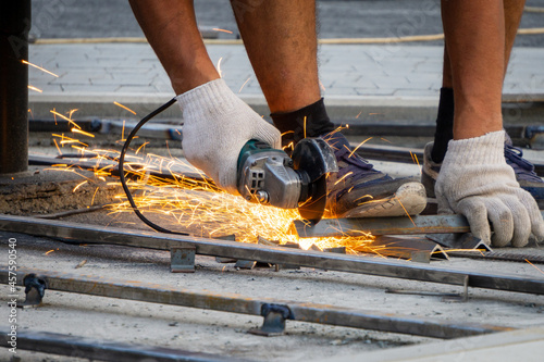 Metal is cut with an angle grinder. Sparks fly away. A man in gloves works with a grinder.