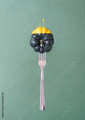 Bilde på lerret Creative composition with silver fork and dark pumpkin dipped in yellow liquid paint against green background