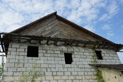 abandoned private white brick house with empty windows with gray wooden loft on a background of blue sky and clouds