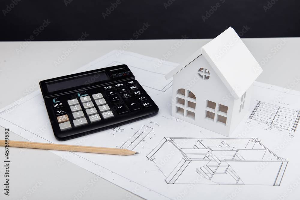 Model of house and calculator on architectural plan. House building costs