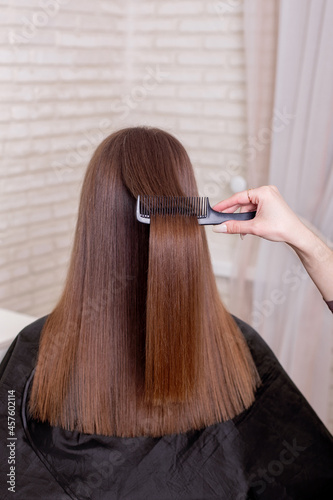 Hairdresser's hand brushing long brunette hair in beauty salon
