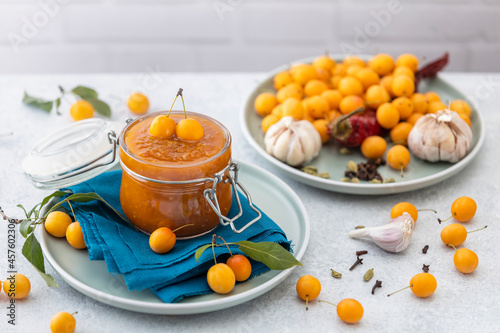 Glass jar of homemade DIY natural canned yellow cherry plum sauce chutney with chilli or tkemali standing on white table photo