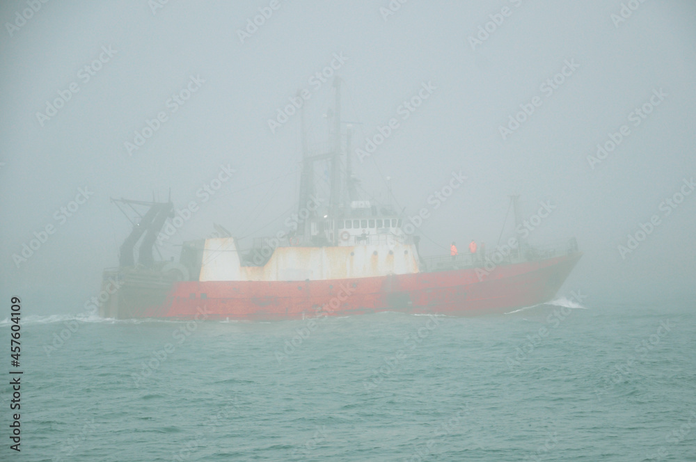 Fishing boat sailing in the ocean through dense fog
