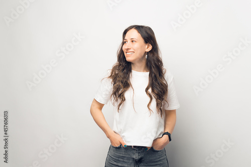 Bright young woman is smiling and looking aside in a white backgrounded studio.