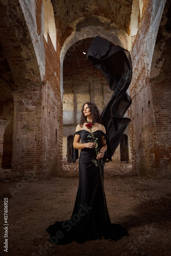Fototapeta Naklejka Na Ścianę i Meble -  A brunette girl with long hair in an evening dress in a vintage Gothic castle. A woman who looks like an evil witch or sorceress in an abandoned old church. Female Model posing in Halloween