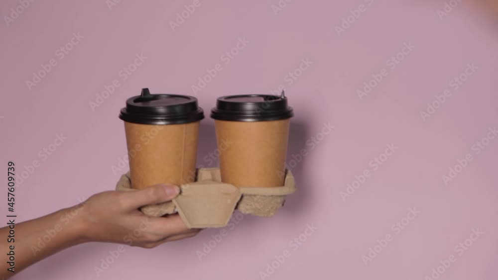 Close-up on a pink background, a woman's hand holds a paper cup with coffee in a stand. Coffee or tea to go. People hands passing one another cup of coffee, coffee delivery.