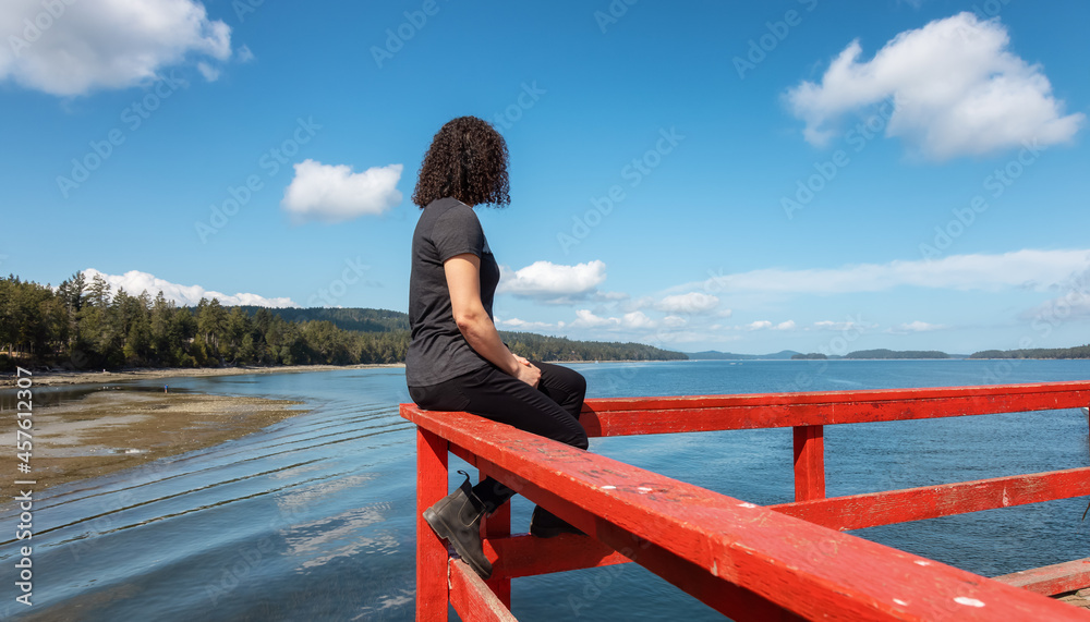 White Caucasian Woman on a Wooden Pier by the Pacific Ocean West Coast. Sunny Summer Day. Fernwood Point Beach, Salt Spring Island, British Columbia, Canada.