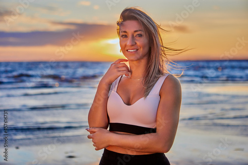 Smiling woman is standing on coast during sunset. © grigvovan