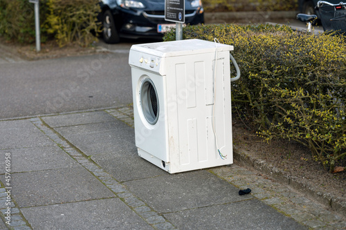 Side view of a washing machine outdoors near a hedge
