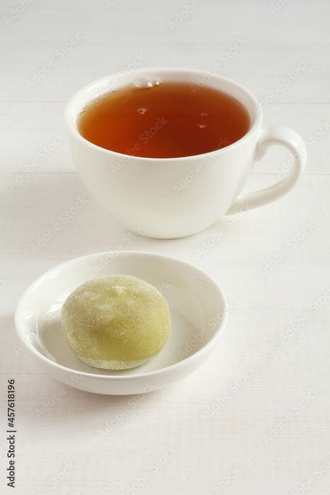 Green matcha tea Japanese dessert mochi on a white saucer and a cup of green tea on a white wooden table. Closeup Green matcha tea Japanese dessert mochi on a white saucer and a cup of green tea on a white wooden table. Closeup