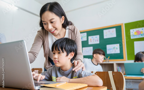 Pupil boy, teacher learn computer in classroom at elementary school. Student boy studying primary school. Children coding online in classroom. Education knowledge, successful teamwork concept banner