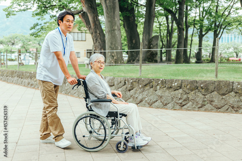 車椅子に乗った高齢者女性と男性スタッフ（全身） 