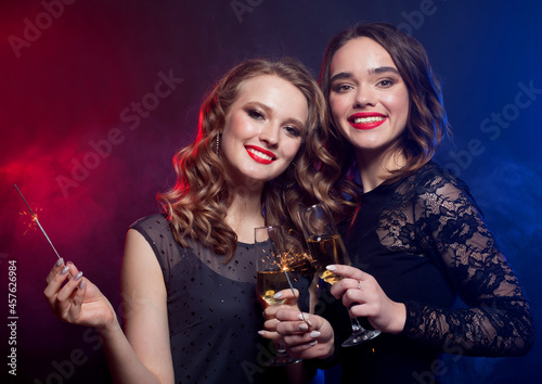 party and people concept - young women clinking flutes with sparkling wine over dark background.
