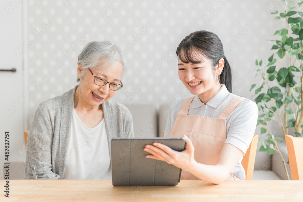 タブレットを使うエプロン姿の女性と高齢者女性
タブレットを使うエプロン姿の女性と高齢者女性