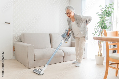 部屋を掃除する高齢者女性（腰痛）
