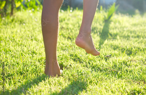 Close-up of child raising legs on green grass with soft light background.