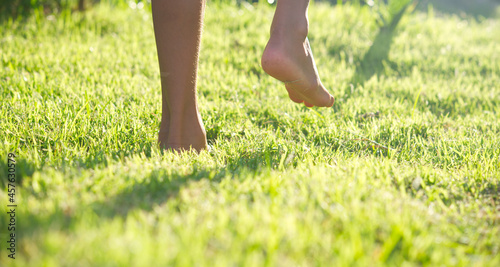 Close-up of child raising legs on green grass with soft light background.
