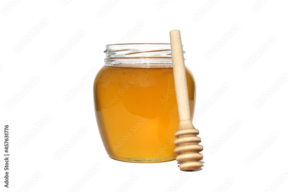 A transparent jar with honey and a wooden spoon stands on a white isolated background. A transparent jar with honey and a wooden spoon stands on a white isolated background.