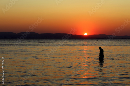 At sunset, a man goes to sea for a swim.